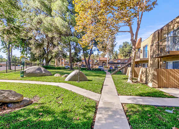 A sidewalk runs through a grassy area with trees and rocks.