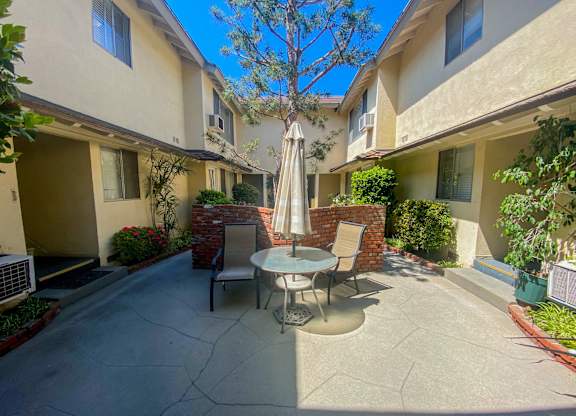 A patio with a table and chairs and a tree in the background.