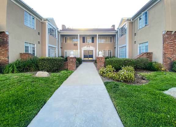 A long concrete walkway leads to a building with a black door and windows.