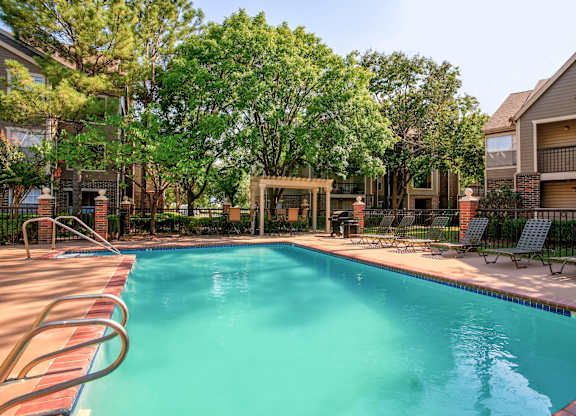 A swimming pool surrounded by trees and chairs.