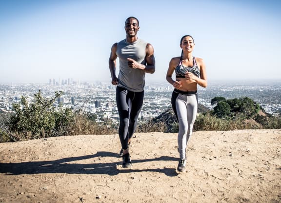 a man and a woman running on a dirt trail with a city in the background
