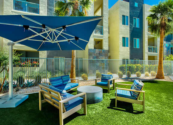 A blue umbrella shades a set of outdoor chairs at Craft at Gilbert and Baseline Apartments, Mesa