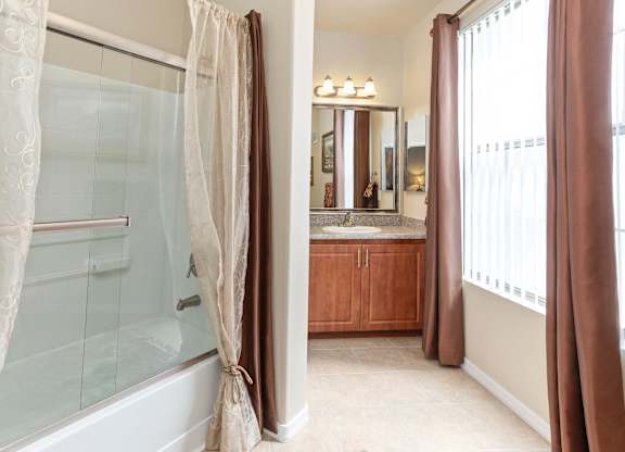 A bathroom with a large mirror and a bathtub with a shower curtain. at Superstition Canyon Apartments, Mesa, AZ, 85209