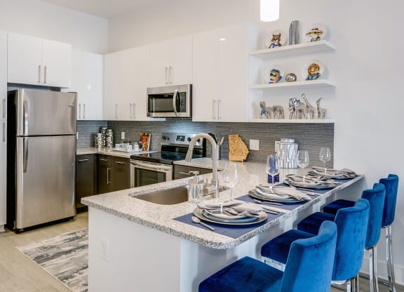 a kitchen with white cabinets and a large island with a granite countertop and blue chairs  at Link Apartments® Mixson, South Carolina
