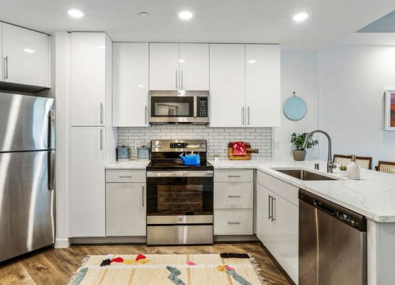 a white kitchen with stainless steel appliances and white cabinets at Link Apartments® Four 12, California