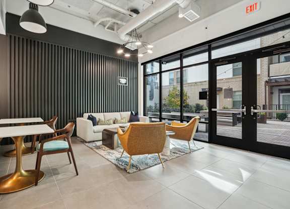 A modern office space with a black vertical blind on the wall, a white sofa, a wooden table, and a yellow chair. at Link Apartments® NoDa 36th Apartments, North Carolina