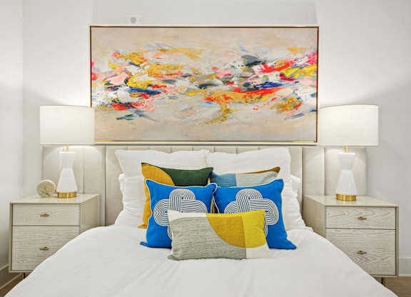 a bedroom with a bed with colorful pillows and a painting above it at Link Apartments® Calyx, Chapel Hill, NC