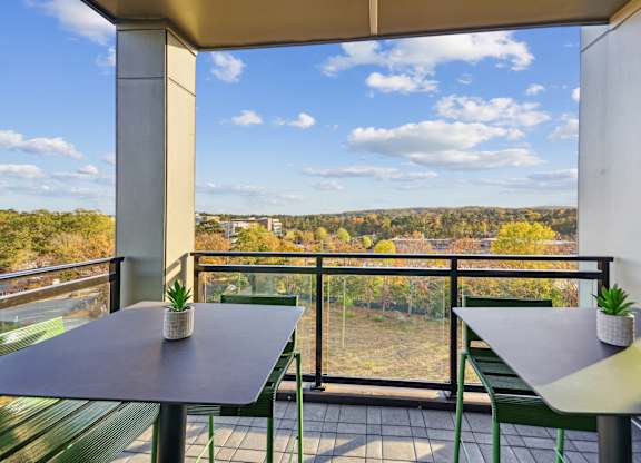 a balcony with tables and chairs and a view of a forest at Link Apartments® Calyx, Chapel Hill, 27517