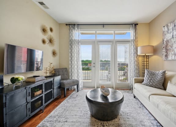 a living room with a couch and a tv and a balcony at Link Apartments® Brookstown, Winston Salem