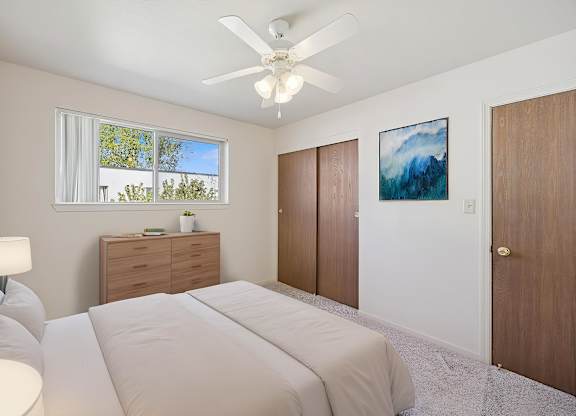 A bedroom with a large bed, a ceiling fan, and a painting on the wall.