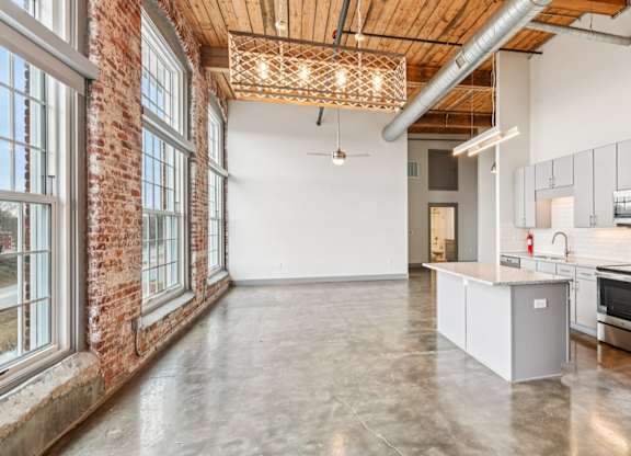 Living room with high ceilings, large windows and kitchen at Converse Mill Loft Apartments in Spartanburg, SC