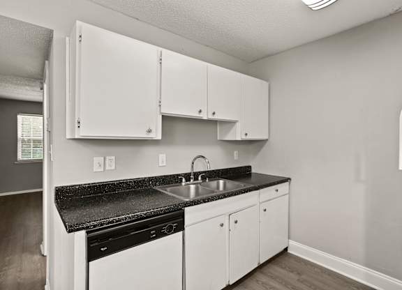 A kitchen with white cabinets and black countertops.