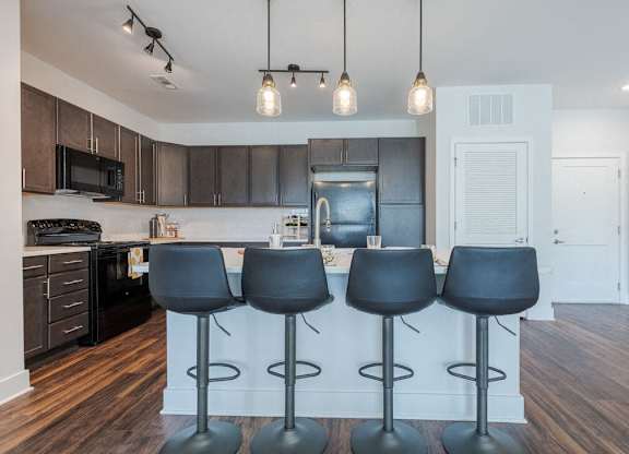 Newry Mill apartments- kitchen with stainless steel appliances including microwave, stove, refrigerator and oven. There is also an island with four barstools in the photo (barstools not included).