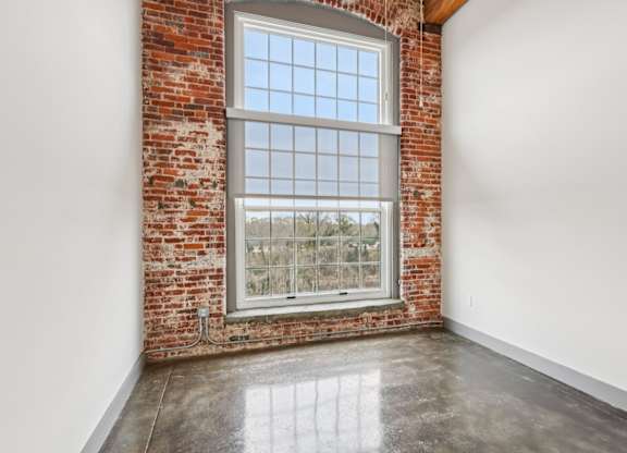 Bedroom in Converse Mill Lofts in Spartanburg, SC with brick walls, high ceilings and large windows.