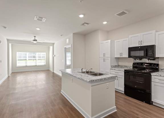 Peaks of Lexington Apartments Kitchen with Black Appliances, Granite Countertops and White Cabinetry and connected living room