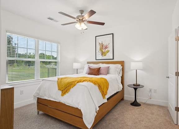 A bedroom with a bed, a ceiling fan, and a window with blinds.