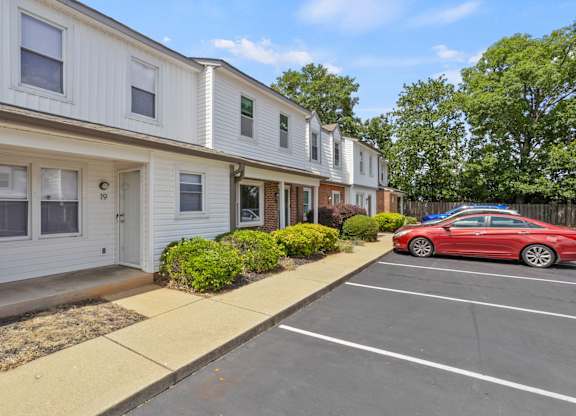 A red car is parked in a parking lot in front of a white building.