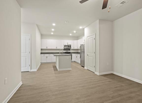 A spacious kitchen with white cabinets and a wooden floor.