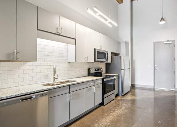 Kitchen with stainless steel appliances, granite countertops, gray cabinetry and stone floors Converse Mill Loft Apartments in Spartanburg, SC
