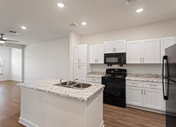 Peaks of Lexington Apartments Kitchen with Black Appliances, Granite Countertops and White Cabinetry and connected living room