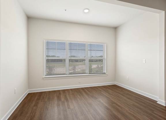 A room with a window covered by blinds and wooden flooring.