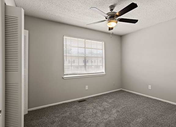 A room with a ceiling fan and a window with blinds.