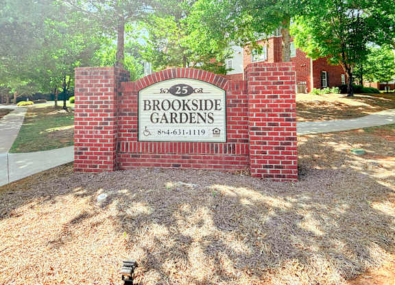 A sign for Brookside Gardens stands in front of a brick wall.