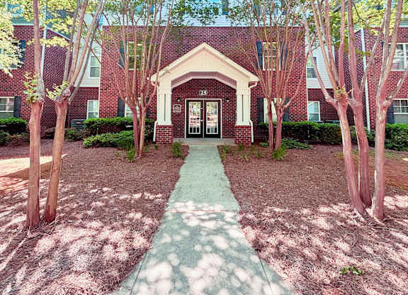 A red brick building with a white door and a green pathway leading to it.