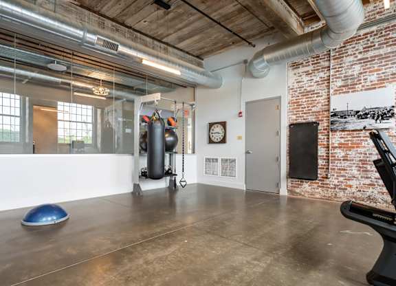 Loft Apartments for Rent in Spartanburg, SC - Converse Mill Lofts - Fitness Center with High Ceiling, Exposed Ductwork and Brick Walls, Large Windows, Large Mirror, Free Weights, and Cardio Equipment.