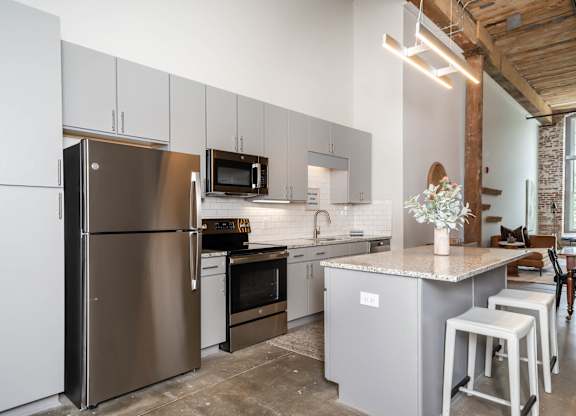 Spartanburg, SC, Loft Apartments Near Hillcrest Market Place - Converse Mill Lofts - Kitchen with Island, Custom Cabinetry, Tile Backsplash, Granite Countertops, and Stainless Steel Appliances.