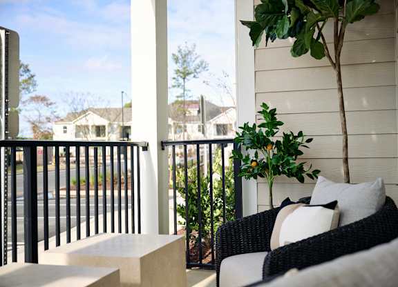 A patio with a black railing, a white couch, and a tree.