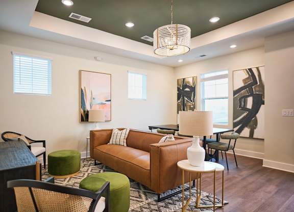 A living room with a brown couch, green ottoman, and a white lamp.