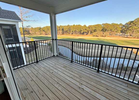 A wooden deck with a black railing overlooks a body of water.