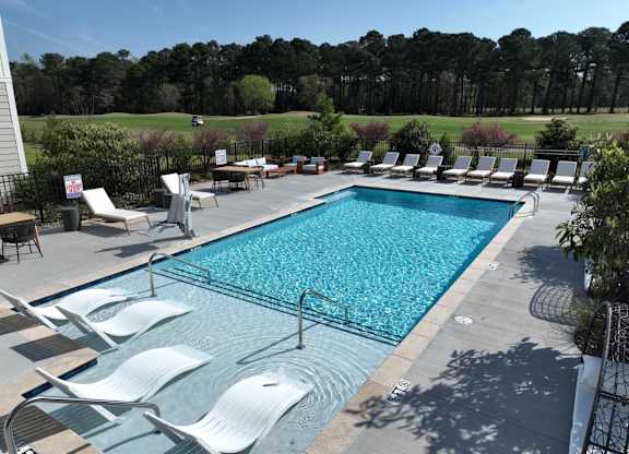 A pool surrounded by chairs and trees.