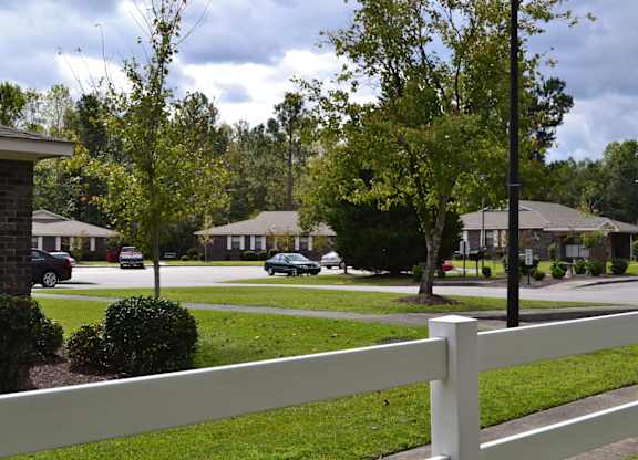 A white fence in front of a grassy area with houses and trees in the background.