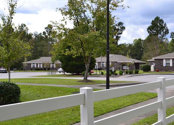 A white fence in front of a grassy area with houses in the background.