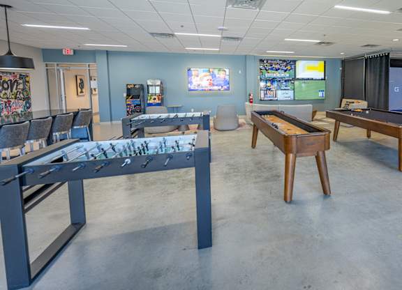 A room with a pool table, a foosball table, and a ping pong table.