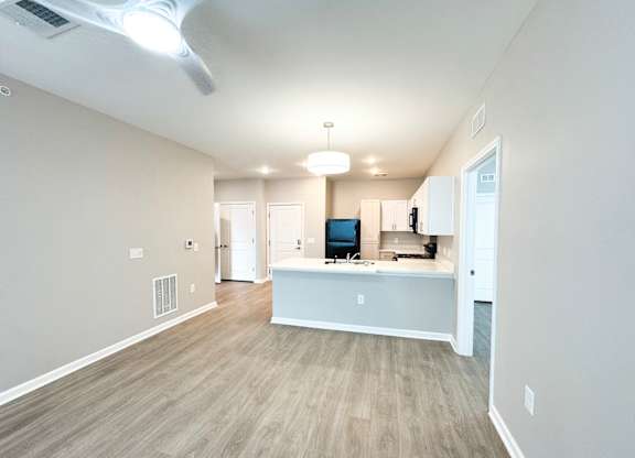 The Haven at Palmer Pointe Senior Apartments living room with luxury vinyl tile flooring, kitchen peninsula, black refrigerator and ceiling fan