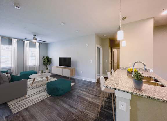 A modern living room with a grey sofa, a white coffee table, a TV, and a kitchen area with a sink and a countertop.