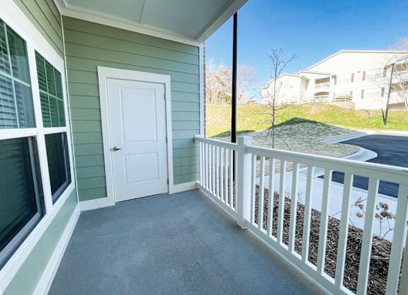 A white door is on the left side of a porch with a white railing.