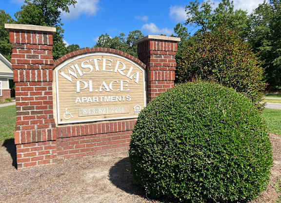 a brick sign for western place apartments in front of a bush