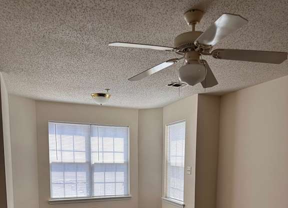 A room with a ceiling fan and two windows.