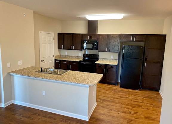 The kitchen of Linden Square apartments, with a granite countertop a black refrigerator, an oven, a microwave and a sink with a disposal.