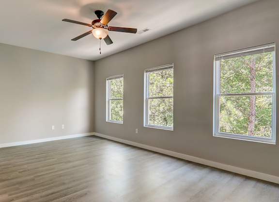 an empty living room with a ceiling fan and three windows