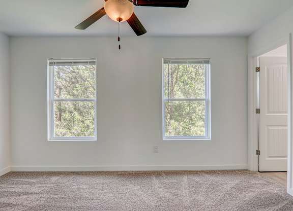 an empty living room with two windows and a ceiling fan