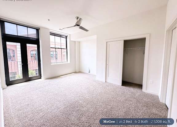 A large, empty bedroom with a ceiling fan and a view of a brick building outside the window.