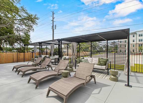 A patio with a black awning and brown chairs.