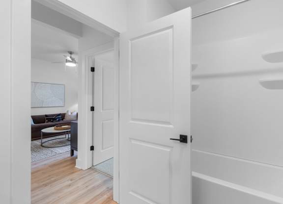 A white door is open to a room with a brown couch and a white wall.