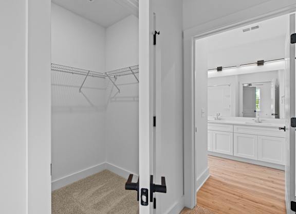 A white closet with a mirror and a bathroom in the background.