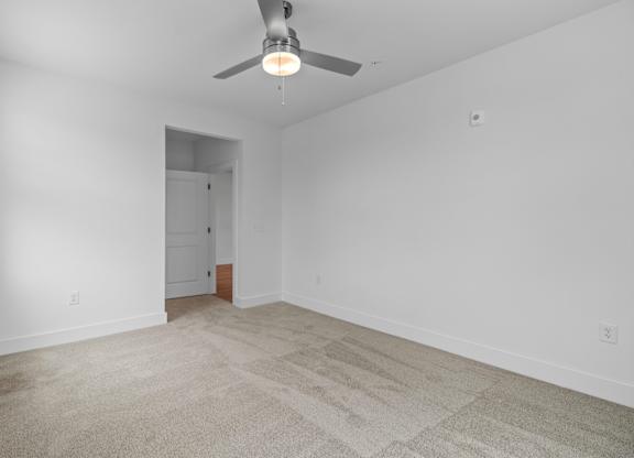 A room with a carpet floor and a ceiling fan.
